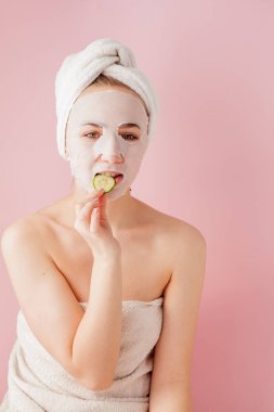 Güzel genç kadın kozmetik doku maske pembe bir arka plan üzerinde bir yüzünde uyguluyor. Sağlık ve güzellik tedavi ve teknoloji kavramı