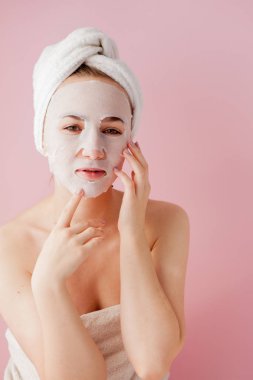 Güzel genç kadın kozmetik doku maske pembe bir arka plan üzerinde bir yüzünde uyguluyor. Sağlık ve güzellik tedavi ve teknoloji kavramı
