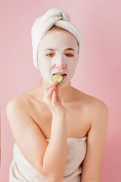 Hermosa mujer joven está aplicando una máscara de tejido cosmético en una cara sobre un fondo rosa. Salud y belleza tratamiento y concepto de tecnología — Foto de Stock