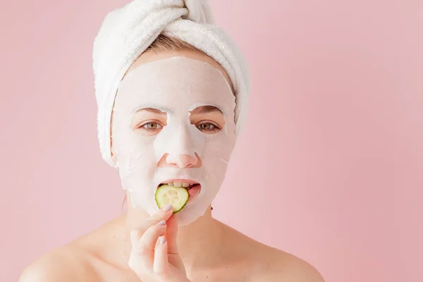 Bela jovem está aplicando uma máscara de tecido cosmético em um rosto em um fundo rosa. Cuidados de saúde e beleza e conceito de tecnologia — Fotografia de Stock