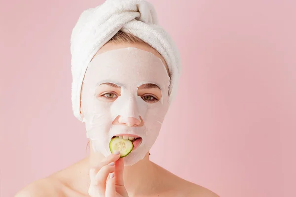 Hermosa mujer joven está aplicando una máscara de tejido cosmético en una cara sobre un fondo rosa. Salud y belleza tratamiento y concepto de tecnología — Foto de Stock