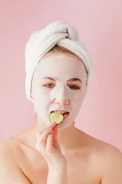 Bela jovem está aplicando uma máscara de tecido cosmético em um rosto em um fundo rosa. Cuidados de saúde e beleza e conceito de tecnologia — Fotografia de Stock