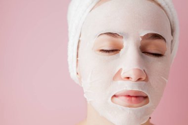 Güzel genç kadın kozmetik doku maske pembe bir arka plan üzerinde bir yüzünde uyguluyor. Sağlık ve güzellik tedavi ve teknoloji kavramı