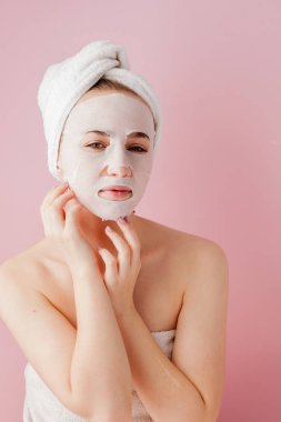 Güzel genç kadın kozmetik doku maske pembe bir arka plan üzerinde bir yüzünde uyguluyor. Sağlık ve güzellik tedavi ve teknoloji kavramı