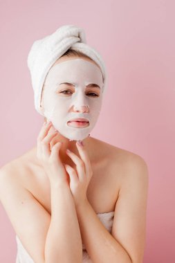 Güzel genç kadın kozmetik doku maske pembe bir arka plan üzerinde bir yüzünde uyguluyor. Sağlık ve güzellik tedavi ve teknoloji kavramı