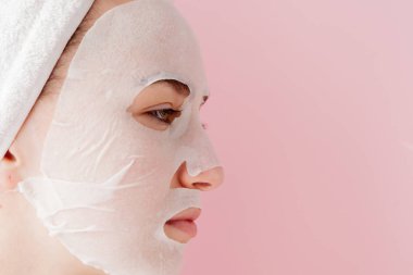 Güzel genç kadın kozmetik doku maske pembe bir arka plan üzerinde bir yüzünde uyguluyor. Sağlık ve güzellik tedavi ve teknoloji kavramı