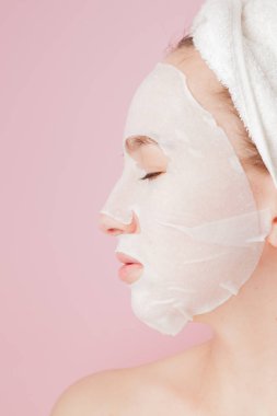 Güzel genç kadın kozmetik doku maske pembe bir arka plan üzerinde bir yüzünde uyguluyor. Sağlık ve güzellik tedavi ve teknoloji kavramı