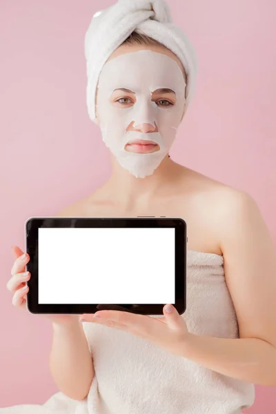Όμορφο κορίτσι με μια μάσκα ιστού και ένα tablet στα χέρια τους με χώρο αντίγραφο σε ροζ φόντο. Υγειονομική περίθαλψη και περιποίηση ομορφιάς και τεχνολογία — Φωτογραφία Αρχείου