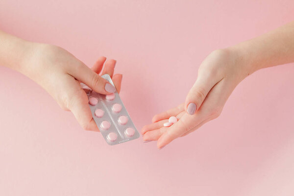 Pink pills tablets in the woman hand on pink background. Top view. Flat lay. Copy space. Medicine concept