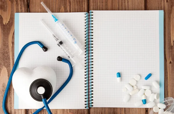 Jeringa, estetoscopio, bloc de notas en blanco y píldora en la mesa del médico. Diagnóstico médico o maqueta de prescripción médica —  Fotos de Stock