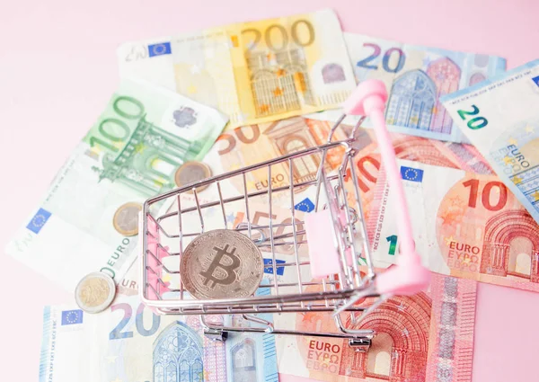 Close up toy shopping cart with bitcoin on a euro background, saving money for future, ethereum cryptocurrency, blockchain business technology concept, pink background for text — Stock Photo, Image