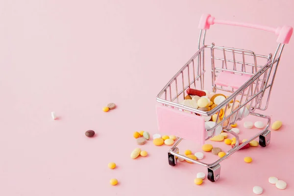 Winkelwagentje uit de supermarkt vol met pillen en drugs op een roze achtergrond. Aankoop van medische preparaten, kopen op het Internet. Plat lag, top uitzicht — Stockfoto
