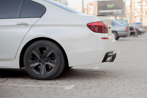 Vista laterale di auto bianca parcheggiata in zona parcheggio pavimentato su sfondo strada periferica offuscata nella luminosa giornata di sole. Concetto di trasporto e parcheggio — Foto Stock