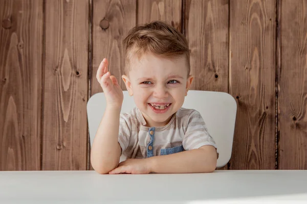 Um menino bonito está sentado na mesa, levantou a mão. Close-up — Fotografia de Stock