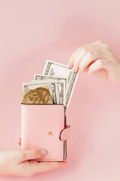 Доллары и розовый бумажник с кредитной картой в руках женщины на розовом фоне — стоковое фото