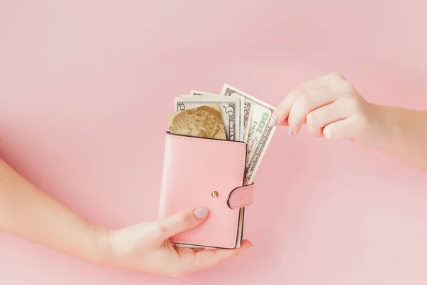 Dollars en roze portemonnee met credit card in handen van de vrouw op roze achtergrond — Stockfoto
