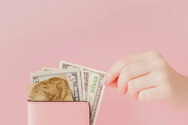 Dollars en roze portemonnee met credit card in handen van de vrouw op roze achtergrond — Stockfoto