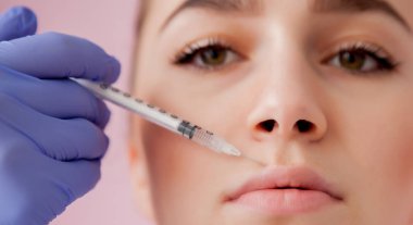 Eldivenli doktor, kadına pembe arka planda dudaklarına botoks yapıyor.