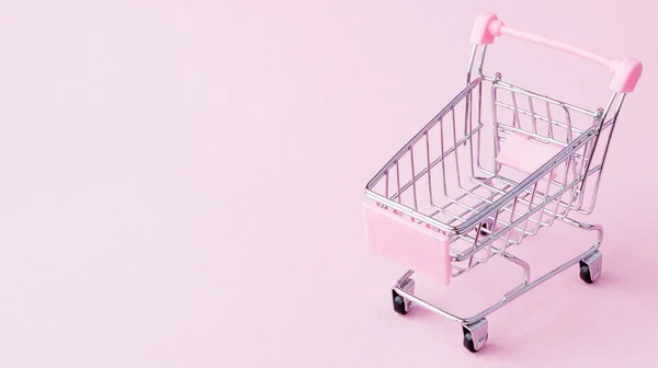 Kis szupermarket élelmiszer push kosár bevásárló játék kerekek és rózsaszín műanyag elemeket, a pasztell rózsaszín papírt lapos feküdt a háttérben. Koncepció a vásárlás. Másolja a hely hirdetés — Stock Fotó
