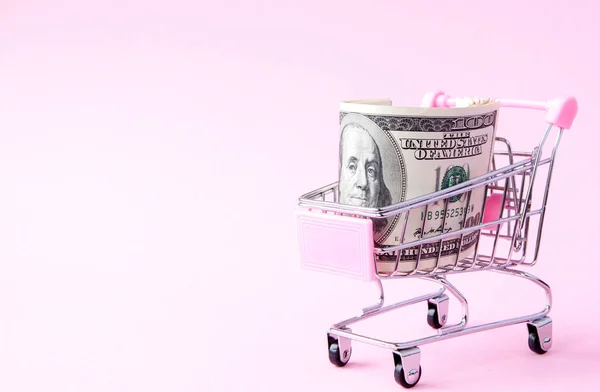 Carrinho de supermercado Cheio de notas de Dólar Americano num fundo rosa com espaço de cópia. Livre comércio. mercado monetário. Estilo minimalista. Um carrinho de compras no supermercado. Venda, desconto — Fotografia de Stock