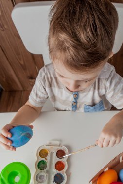 Küçük çocuk renkli yumurta Paskalya için ahşap arka plan üzerinde boyama