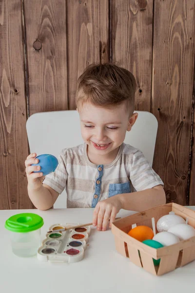 Little boy painting colorful eggs for easter on wooden background — Stock Photo, Image