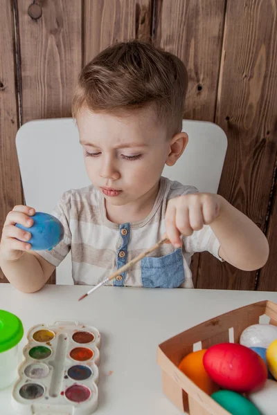 Küçük çocuk renkli yumurta Paskalya için ahşap arka plan üzerinde boyama