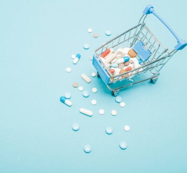 Hap ve mavi arka plan üzerinde alışveriş arabası. Sağlık bakım maliyeti, eczane, sağlık sigortası ve ilaç firması iş kavramı için yaratıcı bir fikir. Kopya alanı