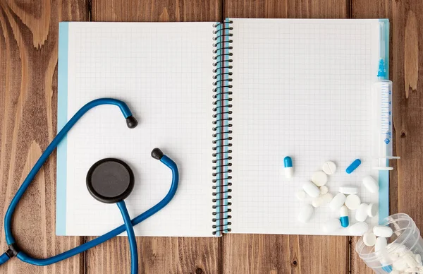 Syringe, Stethoscope, blank page notepad and pill on the doctor table. Medical diagnosis or doctor prescription mockup