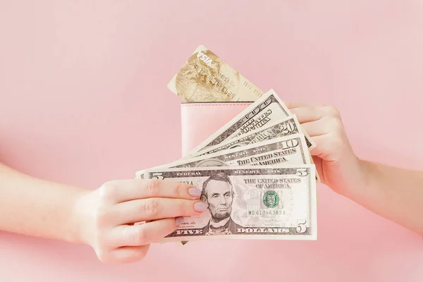 Kyiv, Ukraine - February 22, 2019: Dollars and pink wallet with credit card in woman's hands on pink background — Stock Photo, Image