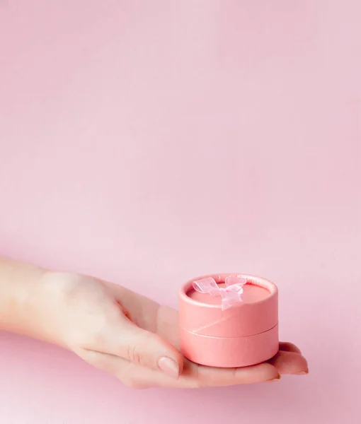 Runda rosa present ask i kvinnors händer på en rosa bakgrund. Festi — Stockfoto