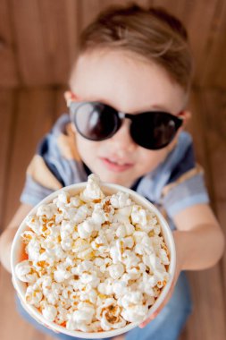 Küçük şirin çocuk bebek çocuk 2-3 yaşında, patlamış mısır, ahşap arka plan üzerinde hızlı yemek yeme için kova tutarak 3d IMAX sinema gözlük. Çocuklar çocukluk yaşam tarzı kavramı. Kopya alanı
