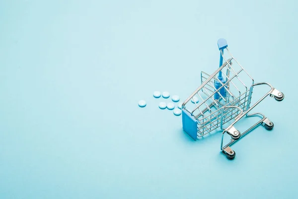 Pillen en Shopping trolley op blauwe achtergrond. Creatief idee voor gezondheidszorg kosten, drogisterij, ziektekostenverzekering en farmaceutisch bedrijf bedrijfsconcept. Kopiëren van ruimte — Stockfoto