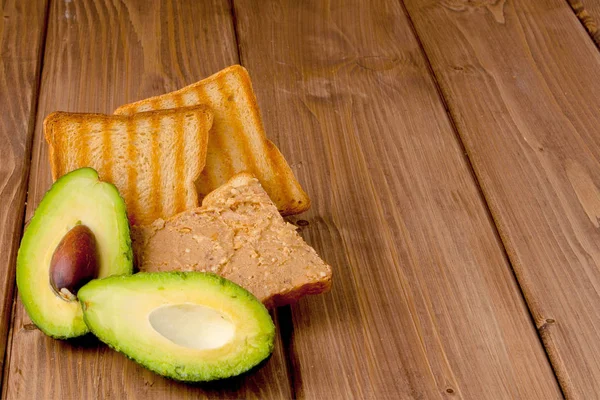 Aguacates y tostadoras con pasta de maní sobre un fondo de madera. Tostadas caseras de desayuno deliciosas y saludables — Foto de Stock