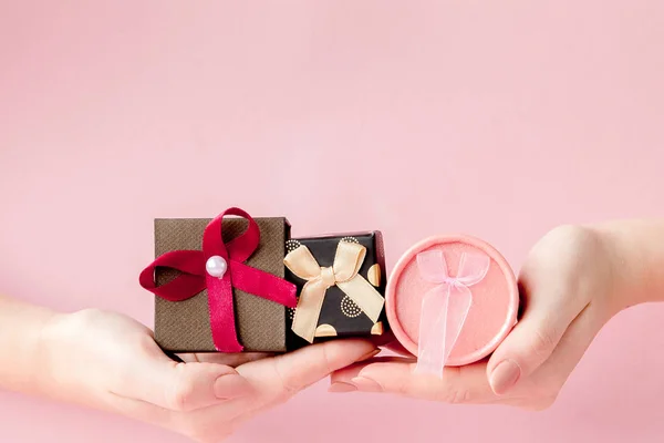 Małe pakiety prezentowe w rękach kobiet na różowym tle. Świąteczny — Zdjęcie stockowe