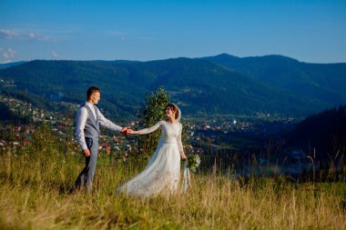 Yeni evliler gülümseme ve diğer her dağın zirvesinde çayır arasında sarıl. Düğün yürüyüş dağlar, nazik duygular çift, Sevgililer günü için fotoğraf ormanda