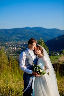 Yeni evliler gülümseme ve diğer her dağın zirvesinde çayır arasında sarıl. Düğün yürüyüş dağlar, nazik duygular çift, Sevgililer günü için fotoğraf ormanda