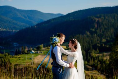Yeni evliler gülümseme ve diğer her dağın zirvesinde çayır arasında sarıl. Düğün yürüyüş dağlar, nazik duygular çift, Sevgililer günü için fotoğraf ormanda