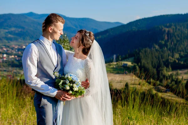 Newlyweds smile and hug each other among the meadow on top of th