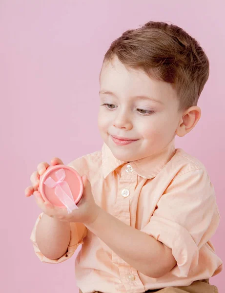 Um rapazinho feliz com um dom. Foto isolada em fundo rosa — Fotografia de Stock