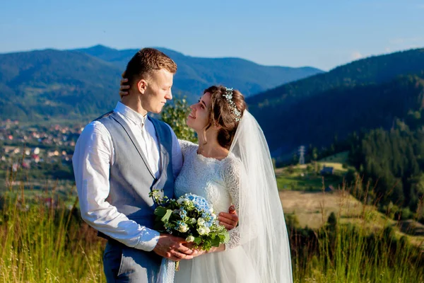 Newlyweds smile and hug each other among the meadow on top of the mountain. Wedding walk in the woods in the mountains, the gentle emotions of the couple, photo for Valentine\'s Day