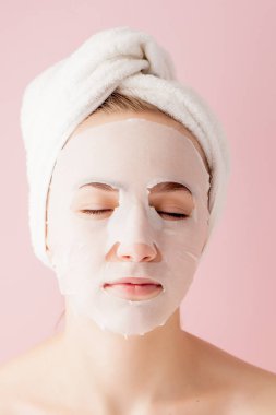 Güzel genç kadın kozmetik doku maske pembe bir arka plan üzerinde bir yüzünde uyguluyor. Sağlık ve güzellik tedavi ve teknoloji kavramı