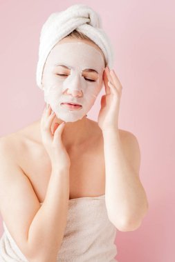 Güzel genç kadın kozmetik doku maske pembe bir arka plan üzerinde bir yüzünde uyguluyor. Sağlık ve güzellik tedavi ve teknoloji kavramı