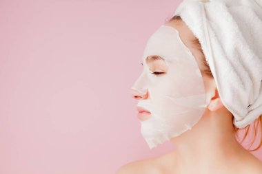 Güzel genç kadın kozmetik doku maske pembe bir arka plan üzerinde bir yüzünde uyguluyor. Sağlık ve güzellik tedavi ve teknoloji kavramı