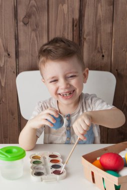 Küçük çocuk renkli yumurta Paskalya için ahşap arka plan üzerinde boyama