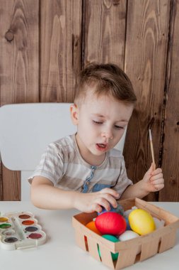 Küçük çocuk renkli yumurta Paskalya için ahşap arka plan üzerinde boyama