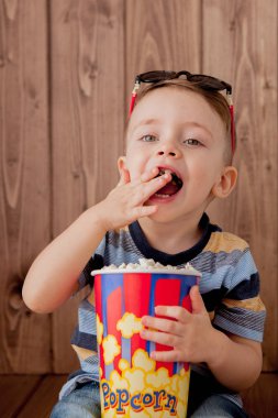 Küçük şirin çocuk bebek çocuk 2-3 yaşında, patlamış mısır, ahşap arka plan üzerinde hızlı yemek yeme için kova tutarak 3d IMAX sinema gözlük. Çocuklar çocukluk yaşam tarzı kavramı. Kopya alanı