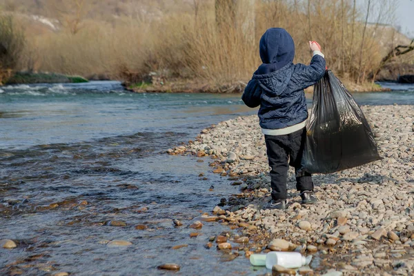 Αποθήκευση έννοια του περιβάλλοντος, ένα μικρό αγόρι συλλογή σκουπίδια και πλαστικά μπουκάλια στην παραλία για να πετάξει στα σκουπίδια. — Φωτογραφία Αρχείου