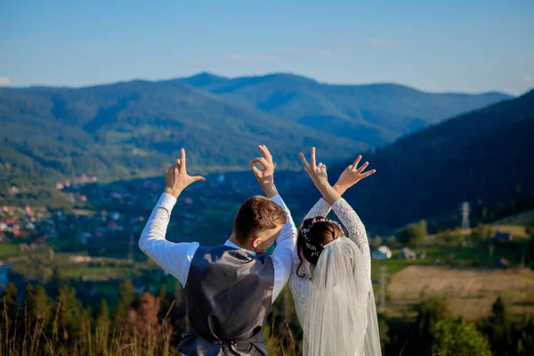 Gli sposi sorridono e si abbracciano tra i prati in cima alla montagna. Passeggiata nuziale nei boschi in montagna, le dolci emozioni della coppia, foto per San Valentino — Foto Stock