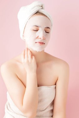 Güzel genç kadın kozmetik doku maske pembe bir arka plan üzerinde bir yüzünde uyguluyor. Sağlık ve güzellik tedavi ve teknoloji kavramı